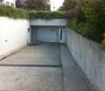 Concrete parking area with garage, plants and shrubs