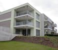 green building, raised ground floor, 5 floors, multiple balconies, ground cover with flowers