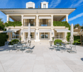 large house with white marble facade, white windows, terrace with tables, plants