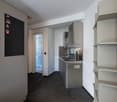 Compact studio apartment with open kitchen, stainless steel appliances including a dishwasher, shelving units, and a blackboard wall for notes or decoration.