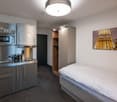 compact room, bed, wardrobe, small kitchenette, silver cabinets, sink, microwave, picture of Eiffel Tower on the wall