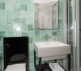 Bathroom with green tiles, white toilet, white sink, glass shower, mirror