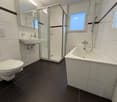 Modern bathroom with glass shower, toilet, sink, bathtub, white tiles, and black floor tiles.