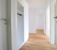 empty corridor with hardwood floor and two doors, white walls, built-in closet with a hanging rod