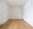 Empty room with white walls, wooden floor, large window, white radiator, white doors