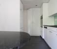 Modern kitchen with granite countertop, black flooring, white cabinets, integrated dishwasher, wall-mounted oven, sink with faucet, and a power outlet