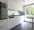 modern kitchen with white cabinets, black countertops, integrated dishwasher and washing machine, faucet, glass table
