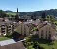 Aerial view of a residential area with multiple houses, some with balconies, surrounded by greenery and mountains