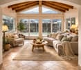 wooden ceiling, large windows, beige tiled floor, two armchairs, central couch, coffee table, center rug, warm lamp
