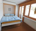 Single bed with blue bedding, glass doors to balcony, wooden wall panels, window, framed artwork