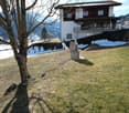 House with balcony, surrounded by snow-covered mountains, grassy field, and a tree