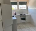White tiled floor, white walls, white cabinets, double sink, electric cooktop, oven, white windows with blinds, outdoor view, white countertop, two open doors, cleaning products on countertop.