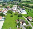 Residential homes with solar panels, driveways, lush green lawns, surrounded by agricultural fields and mountains in the background.