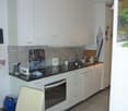 modern kitchen with white cabinets, black countertops, built-in oven, dishwasher, toaster, refrigerator, sink, faucet, and various kitchen utensils