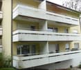 3 story building, yellow exterior, white balconies, multiple windows, metal railings, plants, trees