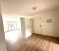 Empty room with wooden flooring, white walls, built-in wardrobe, sliding doors leading to balcony, mounted power outlet, ceiling light, closed door.
