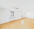 Empty room, white walls, wooden floor, track lighting, windows with shutters, radiators below windows
