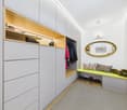 Large walk-in closet with built-in cabinets, shelves, hanging space, bench with pillows, shoes, mirror, wall lamp, and picture frame.