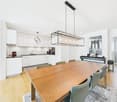 kitchen with modern white cabinets, wooden dining table, chairs, lamps, modern decor, hardwood floors, open balcony