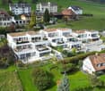 Multiple residential buildings, balconies, green rooftops, gardens, driveways, landscape view