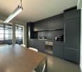modern kitchen with wooden table, black cabinets, stainless steel appliances, large windows