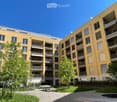 Multi-story apartment building with yellow exterior, balconies, and trees in the courtyard area