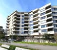 Modern multi-story apartment building with balconies, white exterior, large windows, and a landscaped area in front.