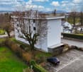 White building, 3 stories, parking lot, car parked, green grass, trees, bushes, road