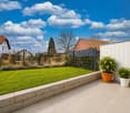 well-maintained garden with green lawn, stone wall, black fence, two potted plants