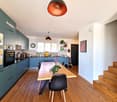 kitchen with dining area, wooden floor, wooden dining table, black chairs, blue cabinets, white walls, ceiling lamps, staircase