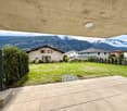 Green grassy field, shrubs, paved walkaway, houses in background, mountains
