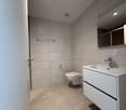 modern bathroom with beige tiles, white vanity, silver faucet, white toilet, wall-mounted mirror
