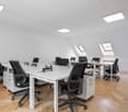 Empty office room with white desk and black chairs, square skylight windows in ceiling.