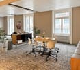 Spacious office space with large windows, beige walls, hardwood floors, round wooden table, swivel chairs, storage cabinet, and potted plants.