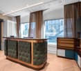 Reception area with a counter, leather seats, wooden bookcases, TV, decorative curtains, wooden floor.