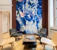 wooden chairs, wooden desk with books, artwork, windows, parquet floor