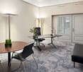 Modern office space with large windows, adjustable desk, comfortable chairs, and decorative elements like plants and lamps.