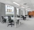 modern office with desks and chairs, large windows, white walls, overhead lights