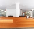 large wooden reception desk, glass office doors, white column, illuminated ceiling lights, white vases, green plant