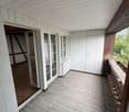 Balcony with glass doors, tiled floor, wooden floor leading to another room, radiator, glass windows