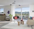 Modern furnished living room, grey tile floor, white rug, windows overlooking scenic landscape, balcony access