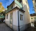 Two-story house, concrete wall, glass balcony railing, windows, entrance door, plants, sidewalk