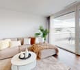 Large windows, balcony with chairs, table, couch with pillows, coffee table, rug, decorative plant, and white walls.