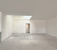 Large open space with white walls, concrete floor, and a doorway visible in the background.