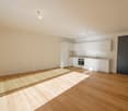 Open-concept studio apartment with hardwood floors, white walls, modern kitchen with white cabinets and appliances, and a bright, spacious living area.
