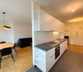modern kitchen, white cabinets, black countertop, gas stove, sink, modern lighting, dining table, chairs, black couch, large mirror