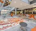 modern lobby with carpet, orange chairs, tables, staircase, glass walls, plants, monitor