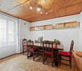 Dining room with wooden table, chairs, wooden cabinet, wooden ceiling, white walls, window with curtains