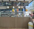 Counter with condiments, menu boards, glass display case, trash bin, coffee machine, and a glass wall.