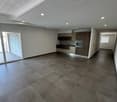 Spacious open-plan living area with large windows, grey tile flooring, modern kitchen with dark wood cabinets and a dishwasher, and recessed lighting throughout the space.